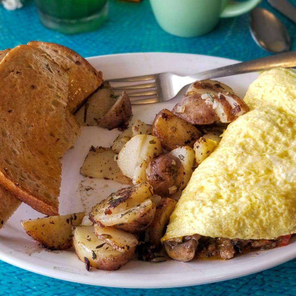Omelet filled with mushrooms, roasted potatoes, and toasted bread slices on a white plate.
