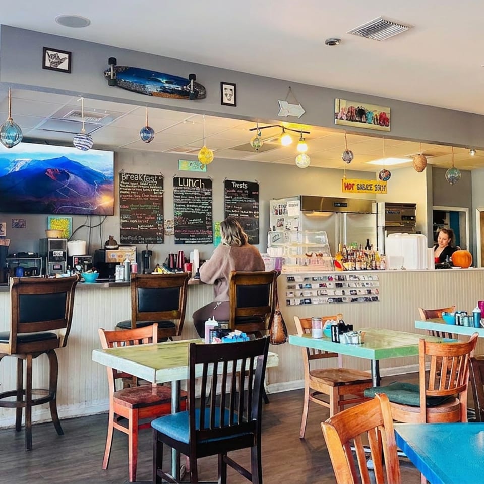 Bright casual restaurant interior with colorful tables, counter seating, chalkboard menus, beverage station, and two diners.